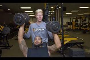 Man lift weights, being spotted by another person.