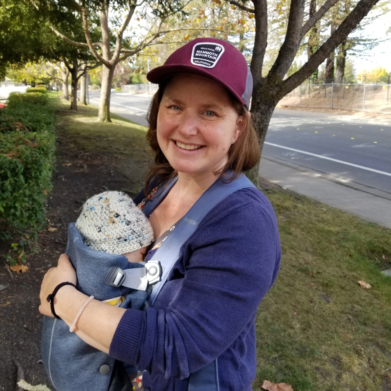 Kandis Longboy Gilmore wearing an infant in a carrier outdoors. 