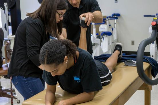 A student and teacher assist another student to correctly bend their knee