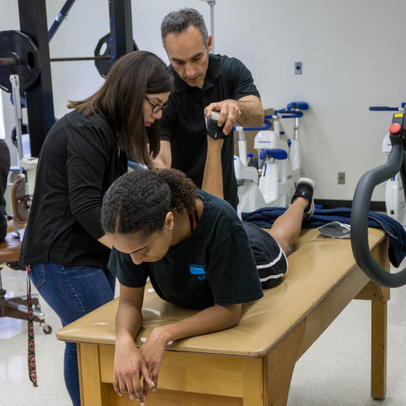 A student and teacher assist another student to correctly bend their knee
