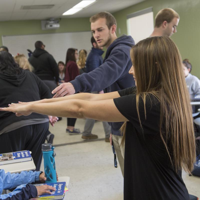 Woman standing with her arms raised, in a Kinesiology class